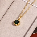 Close-up of golden necklace with deep green birthstone pendant on beige velvet - May Green