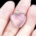 Silver-edged heart pendant with translucent pink gemstone held between fingers - Synthetic Opal Silver Edging