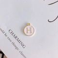 Close-up of pink enamel round charm with golden letter H for DIY jewelry making - Letter H