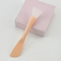 Dual-headed silicone face mask brush and spatula applicator on a pink stand - Orange