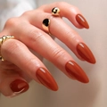 Glossy long almond press-on nails in caramel brown with minimalist gold rings - Flame Orange