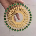 Detailed view of hand holding a large gold circular metal wall decor with green gemstones - Gold Green Zirconia