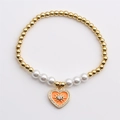 Dettaglio del bracciale elastico con perle dorate e ciondolo a cuore smaltato con occhio - Arancione