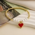 Detailaufnahme von Goldperlen-Armband mit weißer Perle und rotem Herzanhänger auf Stein - Rotes Herz