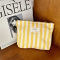 Detail of yellow striped canvas toiletry bag with fabric label on a wooden surface - Yellow