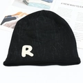 Détail d'un bonnet en maille noire avec bord roulé et écusson lettre R blanc sur fond plat - Taille unique / Noir