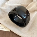 Detail of a wide black acrylic resin bangle with a glossy finish on beige linen fabric - Black