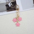 Golden metal keychain with three pink enamel flowers and heart charm on beige fabric - Pink