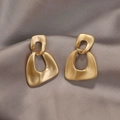 Détail de boucles d'oreilles géométriques dorées mates sur un tissu en satin gris - Géométrie en Or Mat Irrégulier (34#)