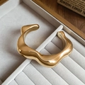Makro-Detail des goldenen Wellen-Armreifs mit poliertem Spiegel-Finish auf Samt-Tablett - Armreif-Gold-Unregelmäßig