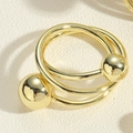 Detailaufnahme eines goldenen mehrlagigen minimalistischen Rings mit polierten Metallperlen - Gekreuzter Kupferperlenring