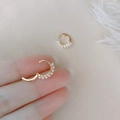 Elegante goldene Creolen mit kleinen Perlen, gehalten vor weichem Federhintergrund - 1 Paar / Gold