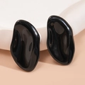 Detailed view of black irregular enamel stud earrings on a white plaster pedestal base - Black