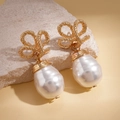 Retro gold bow knot and baroque pearl drop earrings displayed on a natural mineral stone - Gold