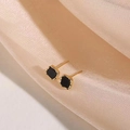 Vista detallada de pendientes cuadrados de esmalte negro y dorado sobre seda champán - Borde Dorado Cuadrado Negro