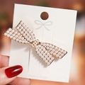 Golden bow hair clip with faux pearls and rhinestones shown on a warm background - Gold Pearl Bow Knot
