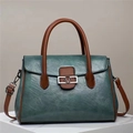 Close-up of vintage leather handbag featuring a V-shaped metal logo and brown handles - Dark Green