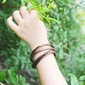 Dettaglio di bracciali intrecciati in bronzo e anelli lisci sul polso con sfondo verde natura - Bracciale rigido intrecciato bronzo vintage (30104)