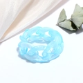 Close-up of a sky blue resin chain ring on white silk with natural leaf accents - Jelly Blue