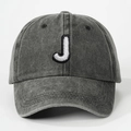 Detailed close-up of a washed grey baseball cap featuring a white embroidered letter J - Letter J