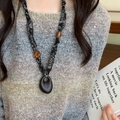 Détail d'un collier ethnique en tissu et perles de bois sur un pull gris doux - Corde En Tissu Floral Noir Perles En Résine Ambre / Style Ovale Noir