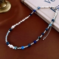 Detalle artístico de collar con cuentas azules, perlas y cadena de plata sobre libros antiguos - Collar de Cuentas de Perlas de Imitación y Piedra de Arena Azul Triangular