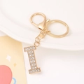 Close-up of golden metal letter I keychain pendant with sparkling rhinestones on ceramic - Letter I