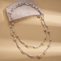 Detalle del collar de perlas de doble capa con cadena plateada sobre piedra rugosa - Blanco