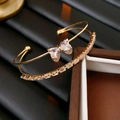 Macro shot of double-layer gold bow bangle with heart zircon stones on a dark background - Gold
