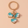 Detail of golden heart keychains with blue enamel inlay and white pearl accents - Blue