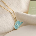 Gros plan d'un collier doré avec pendentif chapeau de cowboy en émail bleu sur tissu blanc - Bleu
