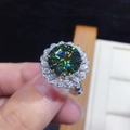 Macro di un anello di lusso con moissanite verde centrale e contorno di diamanti lucidi - Aperto Regolabile / Colore Oro Bianco [3 Carati]