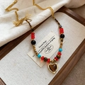Detailed close-up of heart-shaped tiger eye pendant on asymmetric beaded necklace - Gold Red Heart Pendant Style