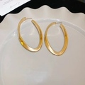 Vue détaillée de boucles d'oreilles créoles ovales dorées torsadées sur une assiette - Doré