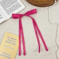 Detail of a bright magenta satin bow hair clip with long ribbons on a white waffle fabric - Rose Red