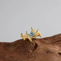 Vista macro dell'anello a onde dorate con topazio blu su un supporto in legno naturale - Anello in oro con topazio naturale