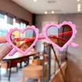 Close-up of pink heart-shaped kids sunglasses with wavy frames and dark lenses - Purple Pink