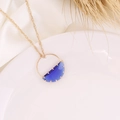 Detailed close-up of a gold necklace with blue crescent pendant on white ceramic plate - Dark Blue