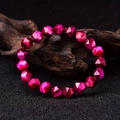 Bracelet en perles d'oeil de tigre facettées magenta sur bois avec un fond sombre - Oeil de Tigre Rose Rouge