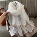 Detalle de bufanda de seda blanca con borde dorado y elegantes adornos de perlas - crema