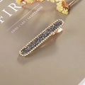 Elegant gold hair clip with dark grey crystals and white rhinestone trim on a book - Rectangular Press Clip / Gray