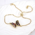 Detail of adjustable gold butterfly bracelet with iridescent crystals on a white ceramic tray - Rainbow