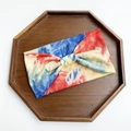 Tie-dye wide knotted yoga headband in red, yellow, and blue patterns on wood tray - Rainbow Tie-dye