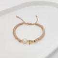 Detail of woven champagne cord bracelet featuring a pearl and golden initial P charm - Letter P