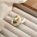Gros plan de créoles dorées en émail blanc sur un coffret à bijoux beige soyeux - Blanc Crème