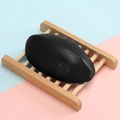 Handmade oval black charcoal soap on a wooden holder with a blue and pink background - 110g Thai-style Bamboo Charcoal Soap