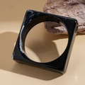 Macro view of geometric black acrylic bangle with white marble texture on stone base - Black