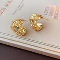 Macro shot of gold C-shaped earrings with irregular folded texture on a book - Gold