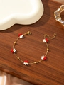 Macro shot of 18K gold-plated flower bracelet with red and white beads on wooden table - Red and White
