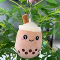 Close-up of a cute milk tea plush keychain with a smiling face and metal ring - 11cm / Brown